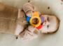 Cute baby chewing on a colorful teething toy while lying on a soft surface.